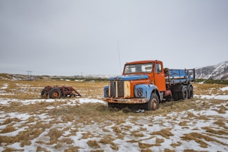 blue and orange stake truck on field near brown farm tractor