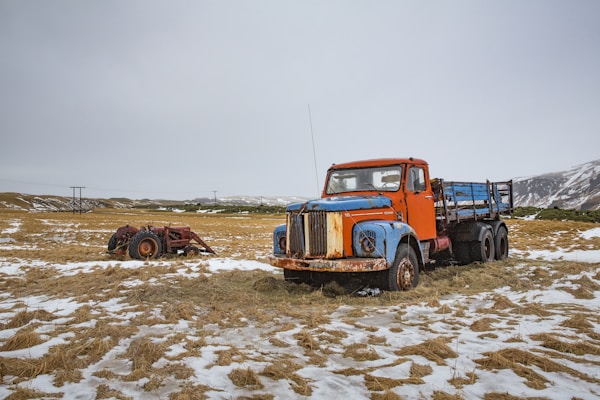blue and orange stake truck on field near brown farm tractor