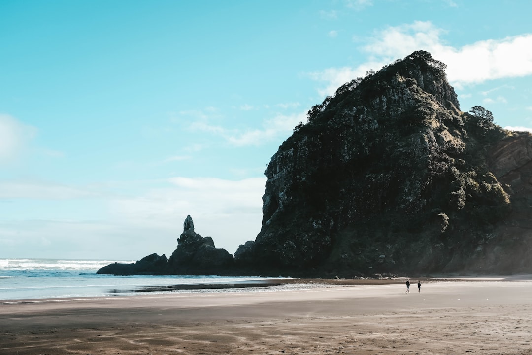 two people walking on shore near gray cliff during daytime