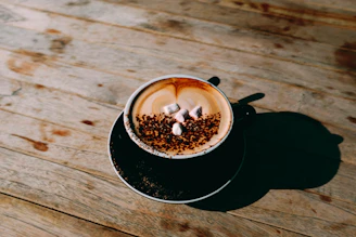 A creamy cappuccino topped with delicate chocolate drizzle and a sprinkle of cinnamon on a sleek black table.