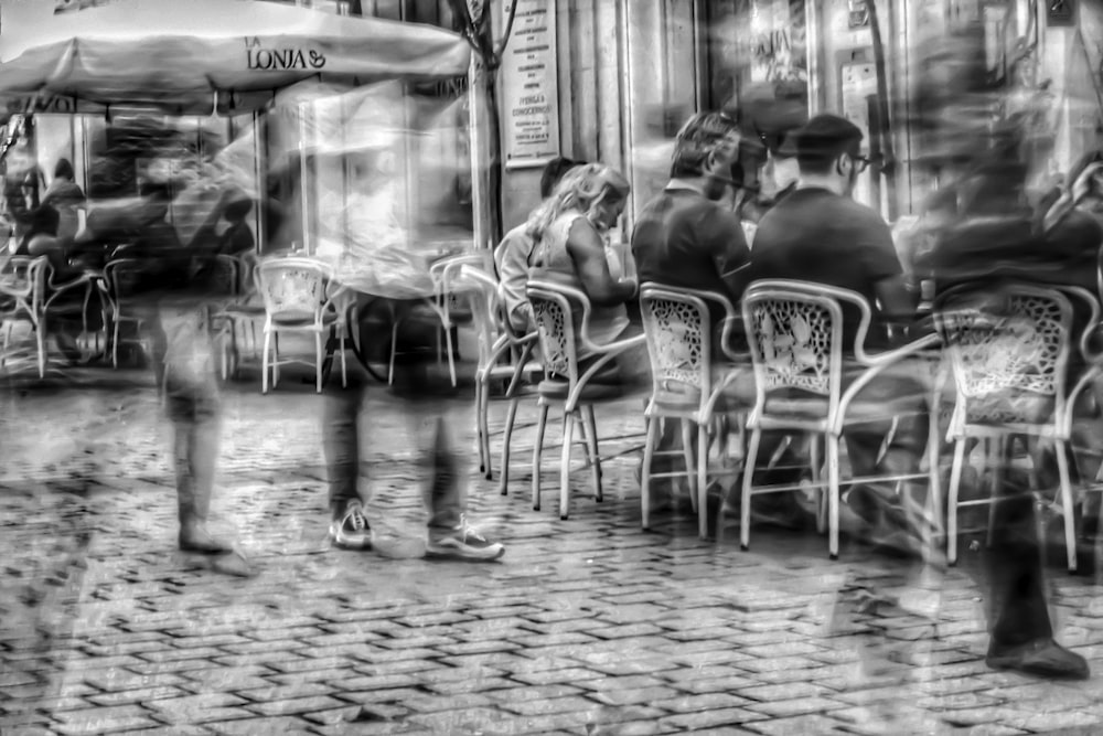 grayscale photography of people sitting on bistro chairs