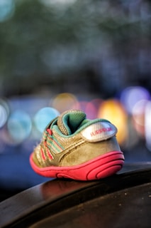 A small child's sneaker placed on a surface, with vivid colors including turquoise and pink. The sneaker is in sharp focus while the background is blurred, featuring bokeh lights in various colors.