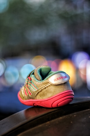 A small child's sneaker placed on a surface, with vivid colors including turquoise and pink. The sneaker is in sharp focus while the background is blurred, featuring bokeh lights in various colors.