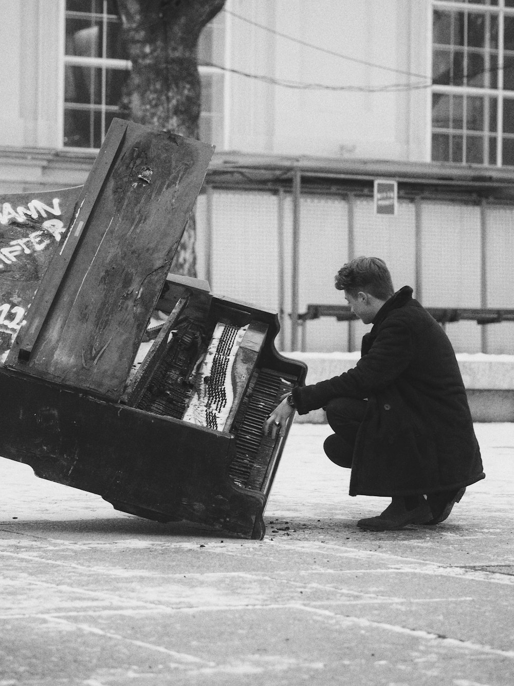 grayscale photography of man crouching in front of damaged piano