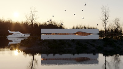 A modern white building with a sleek design sits by a calm river, surrounded by barren trees. The sunset casts warm light, contrasting with the building's minimalistic architecture. Birds are flying above, and a luxury yacht is seen on the water.