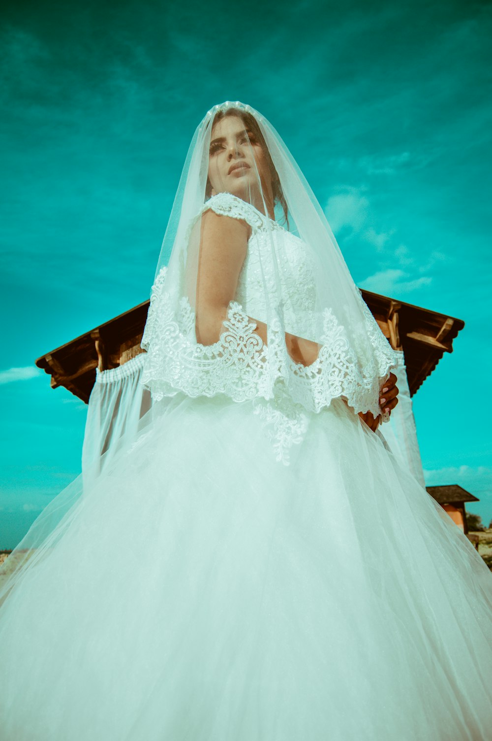 Photographie en contre-plongée d’une femme en robe de mariée blanche près d’un hangar brun pendant la journée