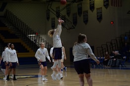 Men's basketball training session with players shooting hoops in a gym.