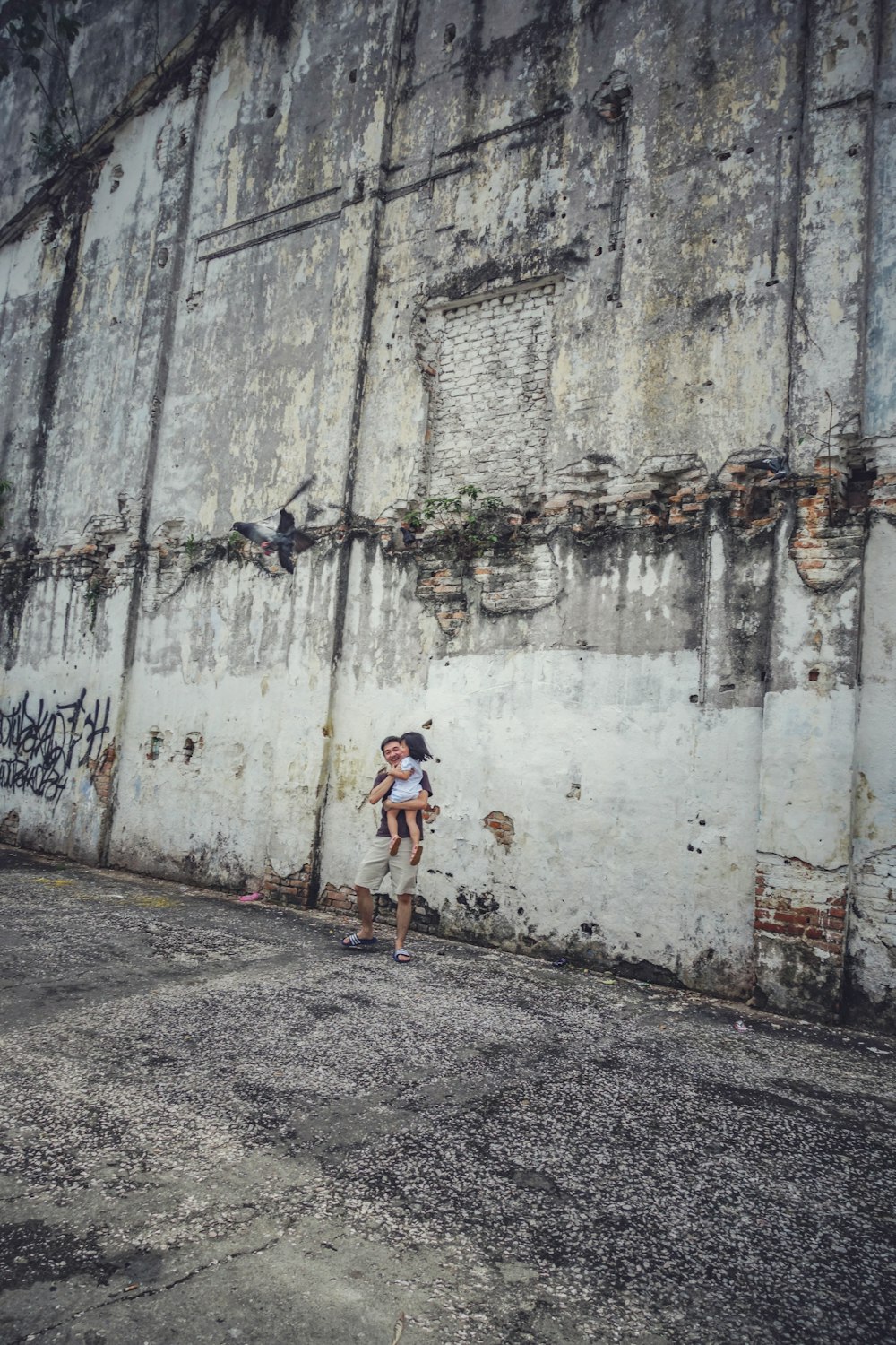 man carrying girl near gray concrete wall