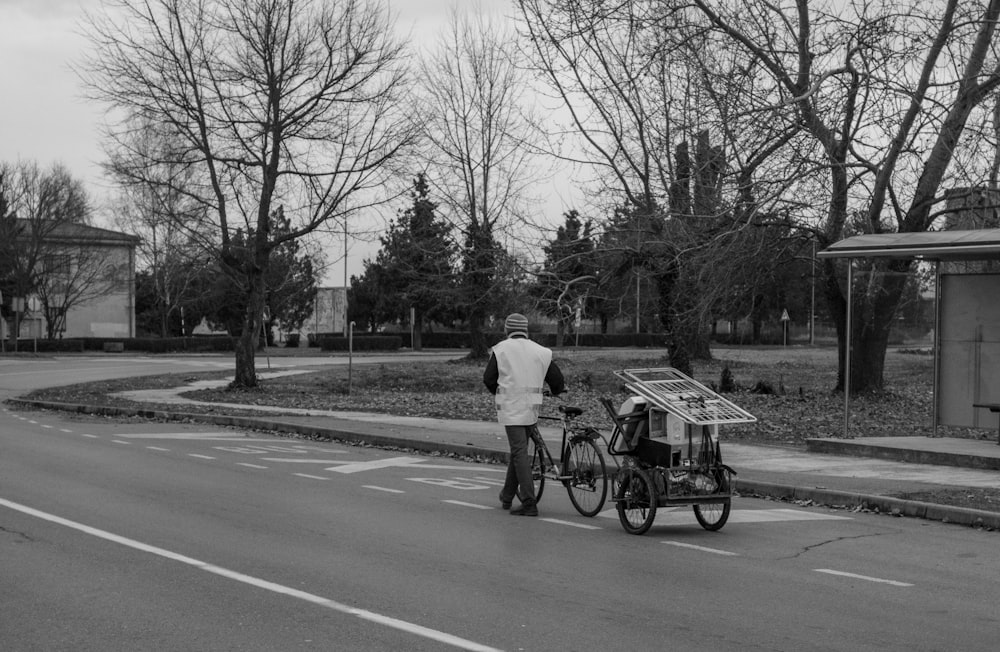 Foto en escala de grises de una persona caminando al lado del triciclo