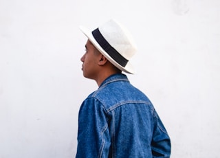 man wearing blue denim jacket and white fedora while standing