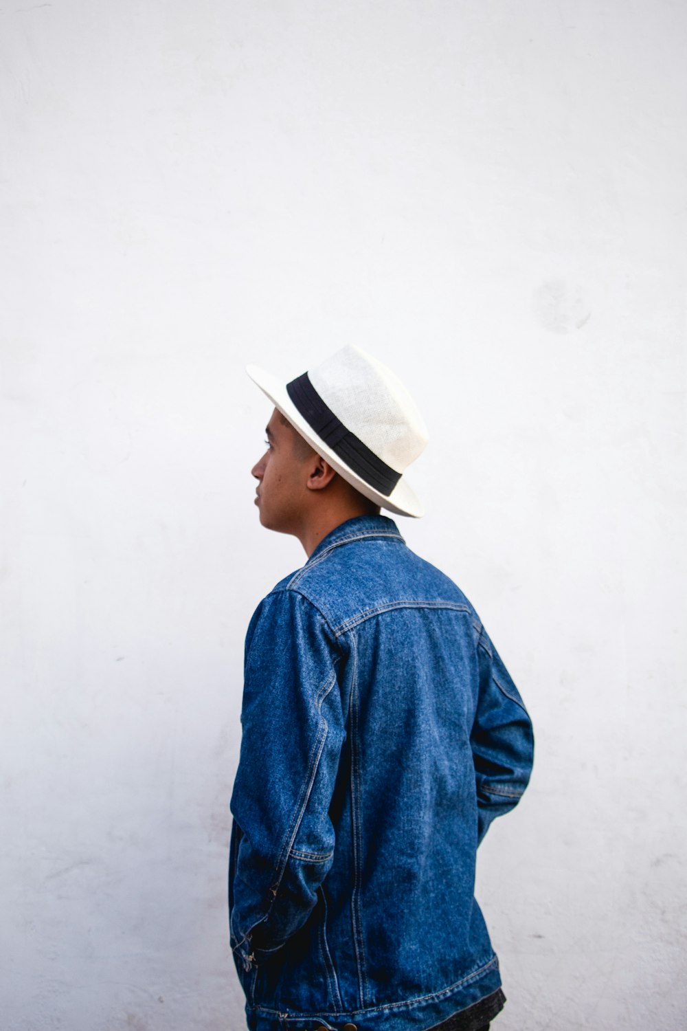 man wearing blue denim jacket and white fedora while standing