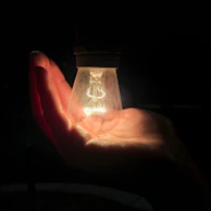 Close-up of a robotic hand gently holding a glowing brain-shaped light bulb.