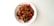 A bowl of stir-fried vegetables and strips of meat, possibly chicken or beef, are arranged on a white plate. The dish includes sliced carrots, bell peppers, onions, and a scattering of crushed nuts or seeds on top. The background is a simple, clean white surface.