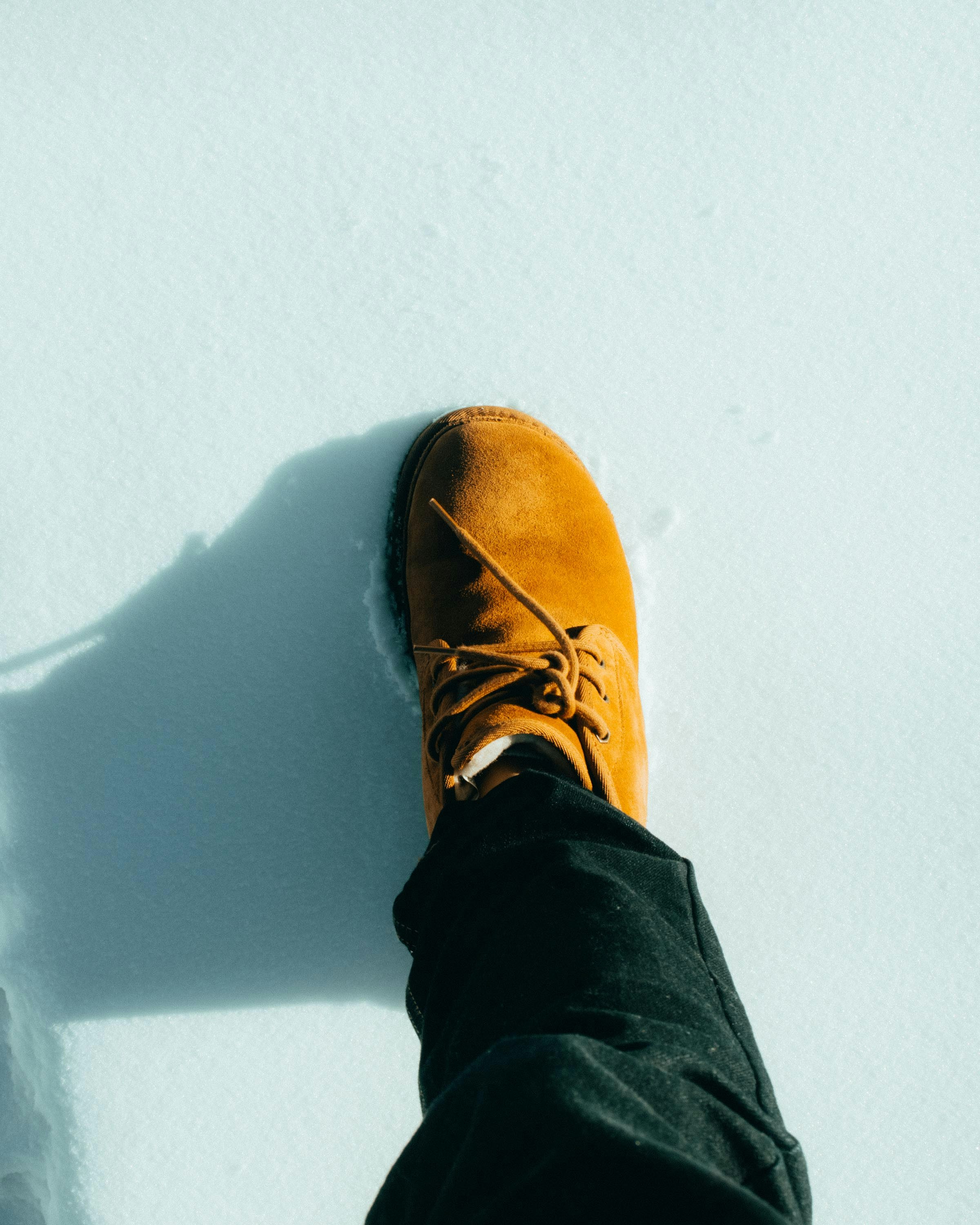 high angle photography of brown shoe stepping on snow field