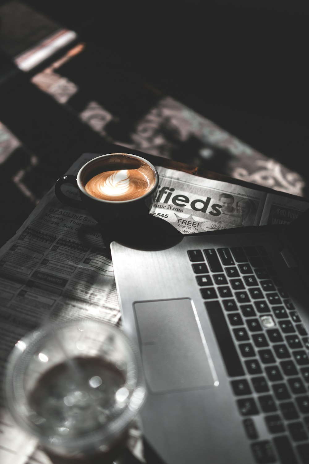 ラップトップコンピュータの横でコーヒーで満たされたマグカップの選択的カラー写真
