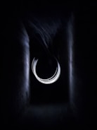 A dark tunnel-like structure with a central circular light pattern that appears abstract and ethereal. The light swirls in a concentric manner, creating an illusion of a portal or vortex.
