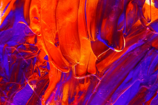 Bold and vibrant abstract artwork featuring dynamic swirls and streaks of bright red and deep blue colors. The thickly applied paint creates a textured, almost three-dimensional effect, with a mix of smooth and rough surfaces.