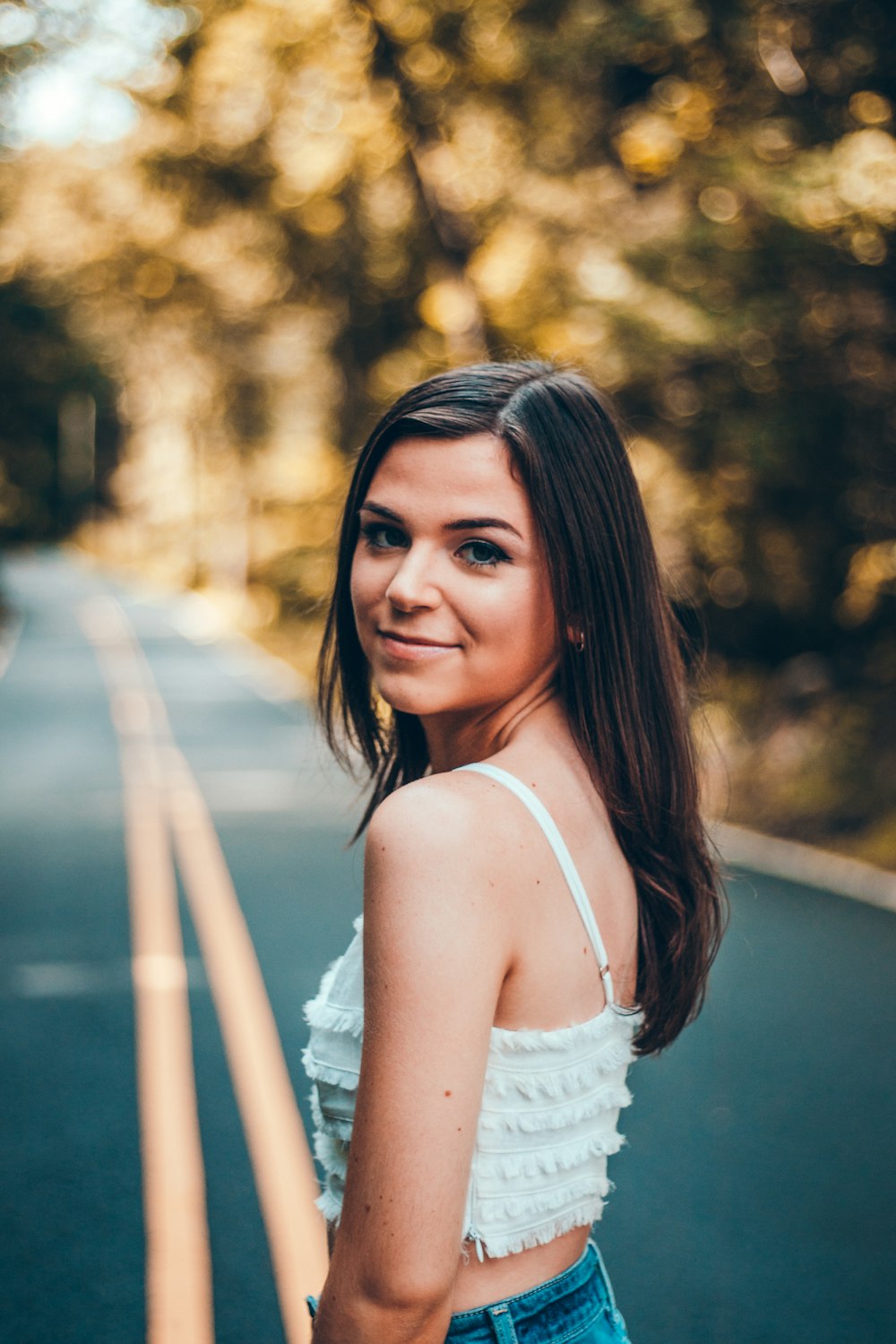 selective focus photography of woman standing on road between trees