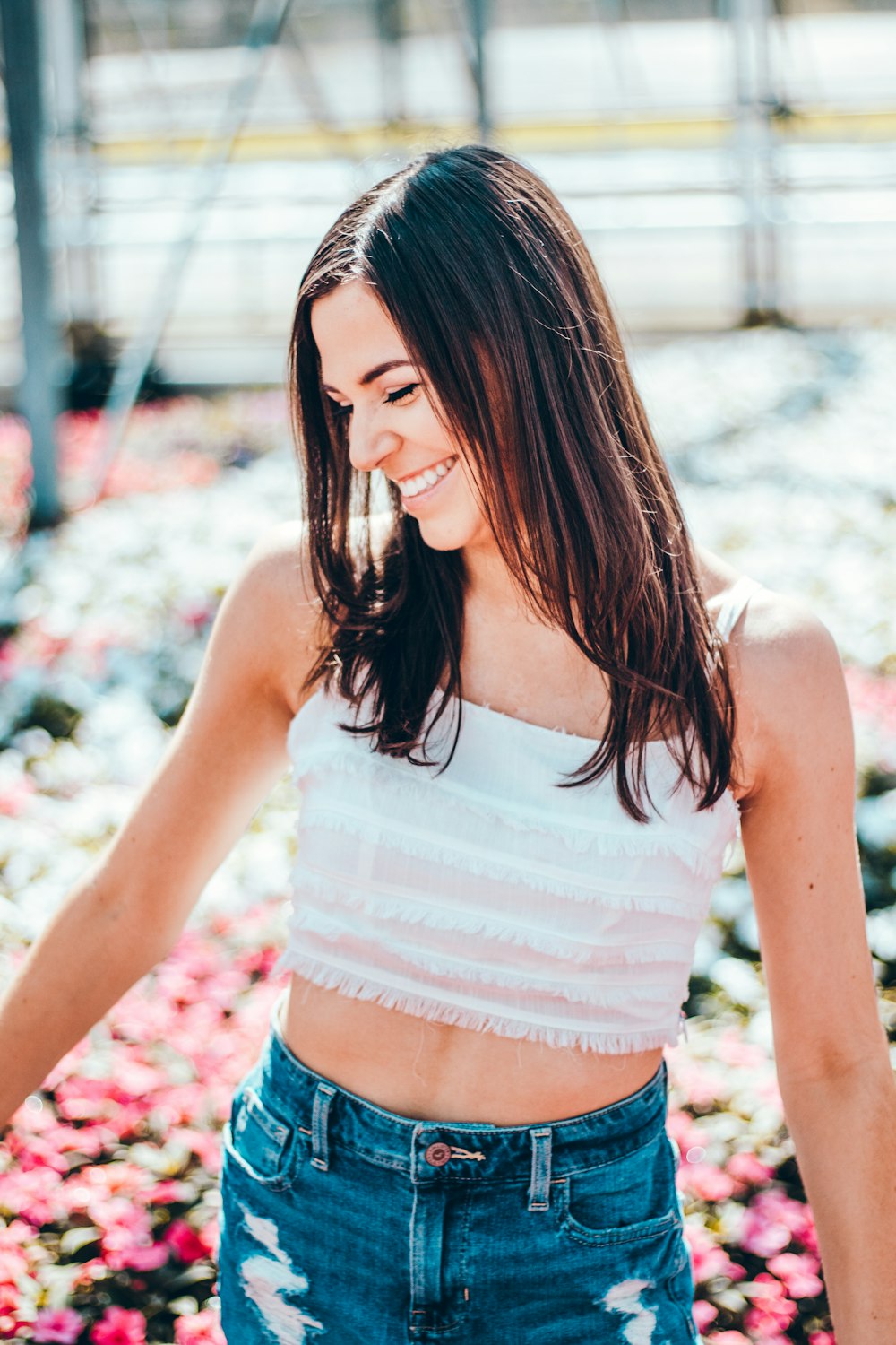 woman in white spaghetti strap crop top smiling and standing surrounded with pink flowers during daytime