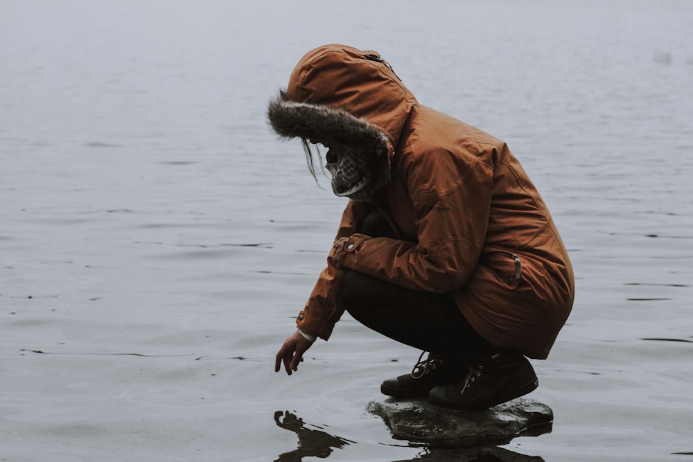 person on rock trying to touch body of water