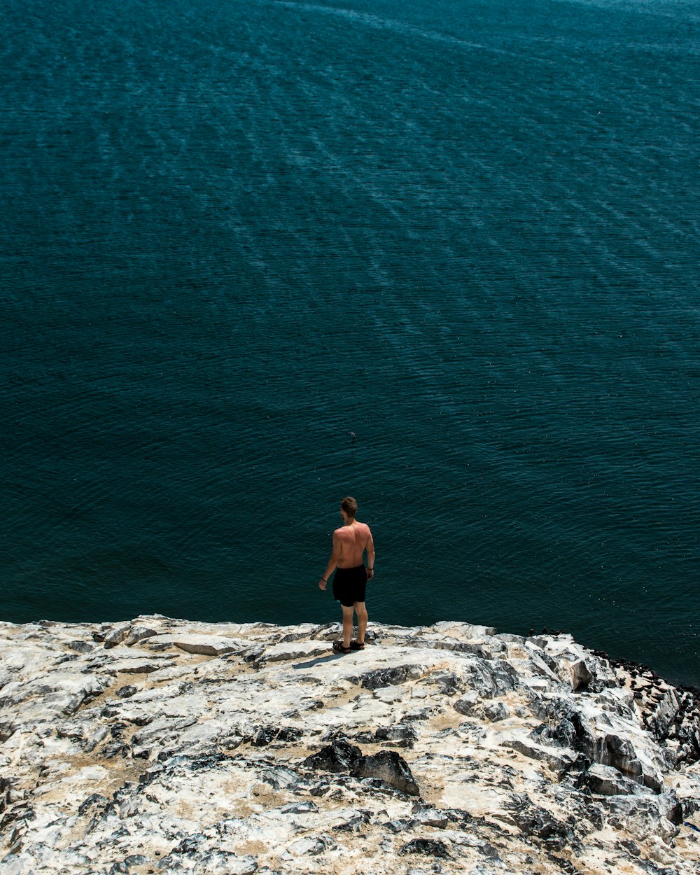Persona de pie en el borde de un acantilado sobre un cuerpo de agua que mira