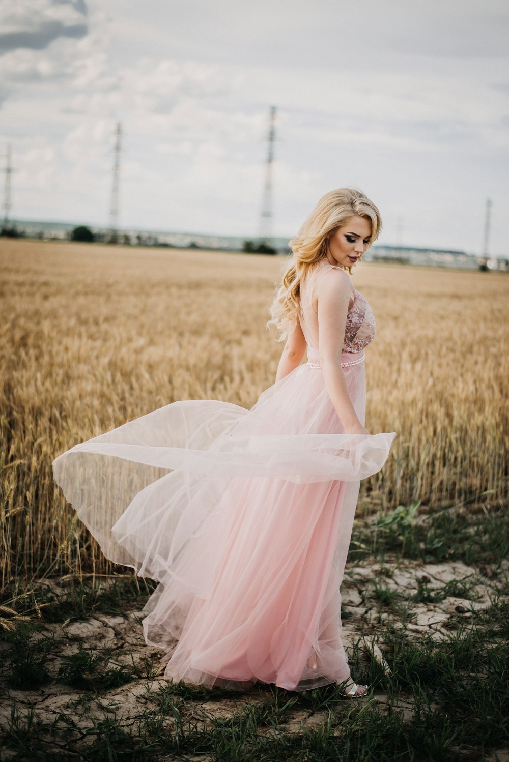小麦畑のそばに立つピンクのエンパイアウエストドレスを着た女性