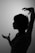 A silhouette of a person with short hair and expressive hand gestures, set against a plain background. The person's profile and hands are sharply defined, creating a dramatic contrast.