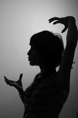 A silhouette of a person with short hair and expressive hand gestures, set against a plain background. The person's profile and hands are sharply defined, creating a dramatic contrast.