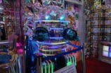 A highly reflective robot with a spherical head and glowing blue and green lights. The environment features colorful and intricate patterns with mirrored surfaces and geometric designs. There is a sign with text in front of the robot, and the walls display colorful, cartoonish tiger illustrations.