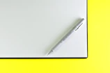 Square image of a pastel yellow notebook with a pen resting on top.