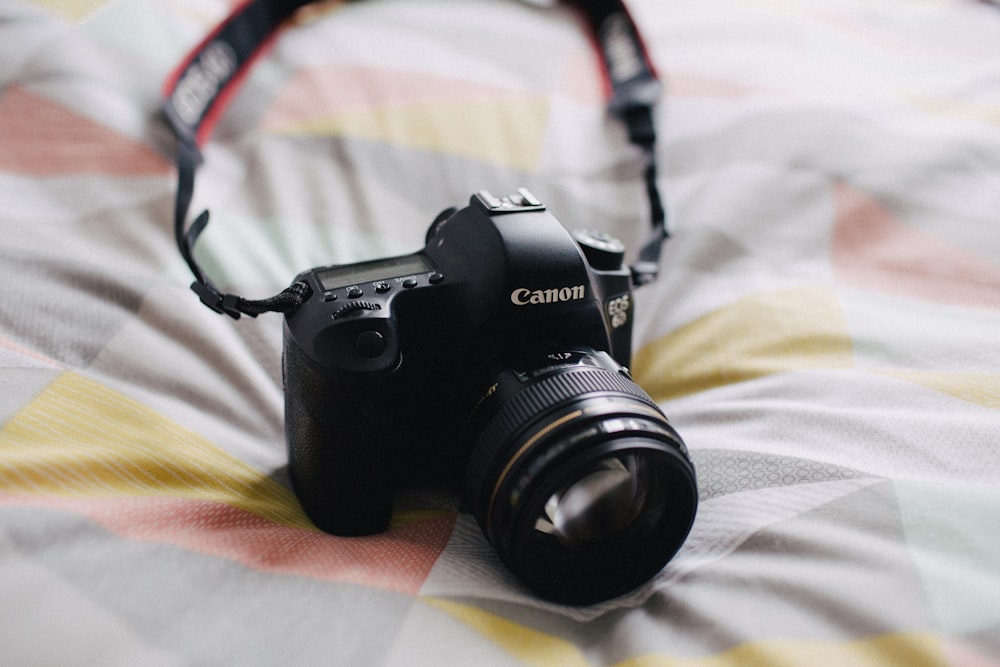 black Canon DSLR camera on white, gray, and yellow textile