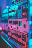 A close-up view of vintage audio equipment with various knobs, dials, and meters. The lighting casts a vibrant, colorful glow, enhancing the details of the metallic and plastic components.