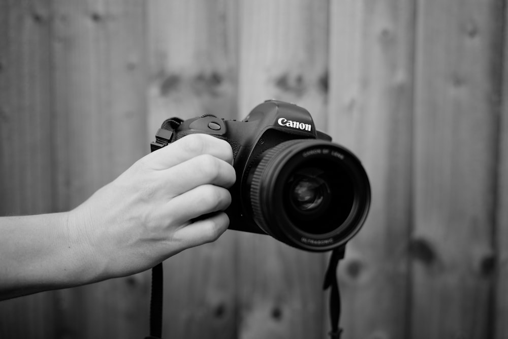 grayscale photography of person holding Canon DSLR camera