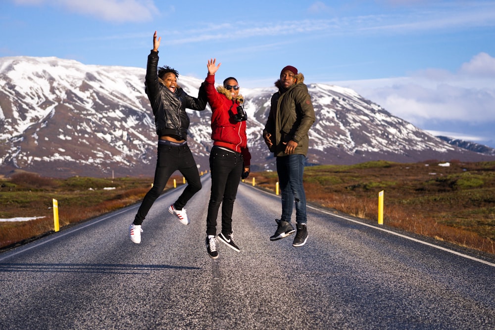 three men jumping on road at daytime