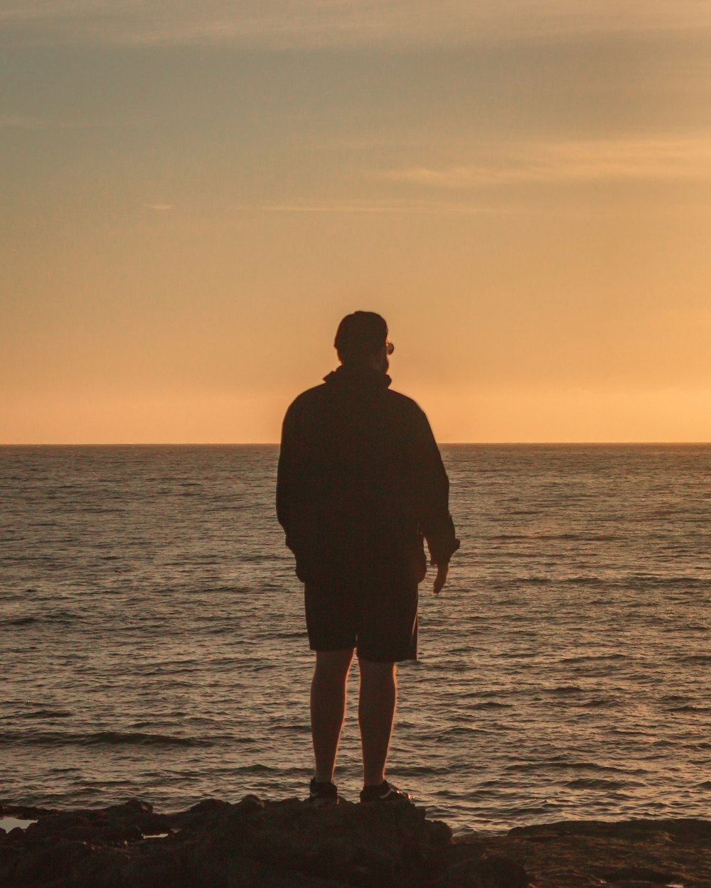 man standing while overlooking body of water during golden hour