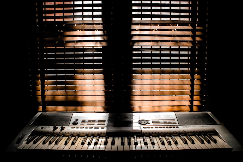gray electronic keyboard placed in front of window blinds
