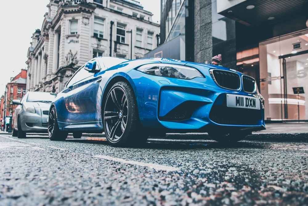 blue BMW coupe parked on roadside in front of building
