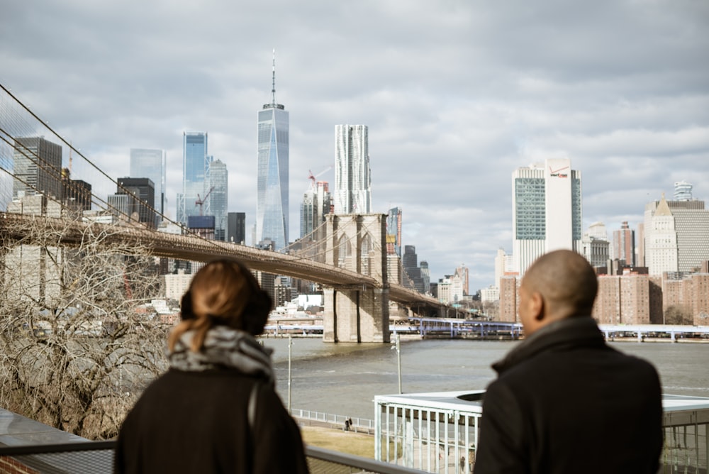 homme et femme debout devant un plan d’eau, un pont et des bâtiments