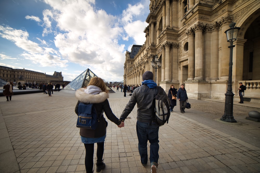 man and woman holding hands while walking on gray concrete ground during daytime