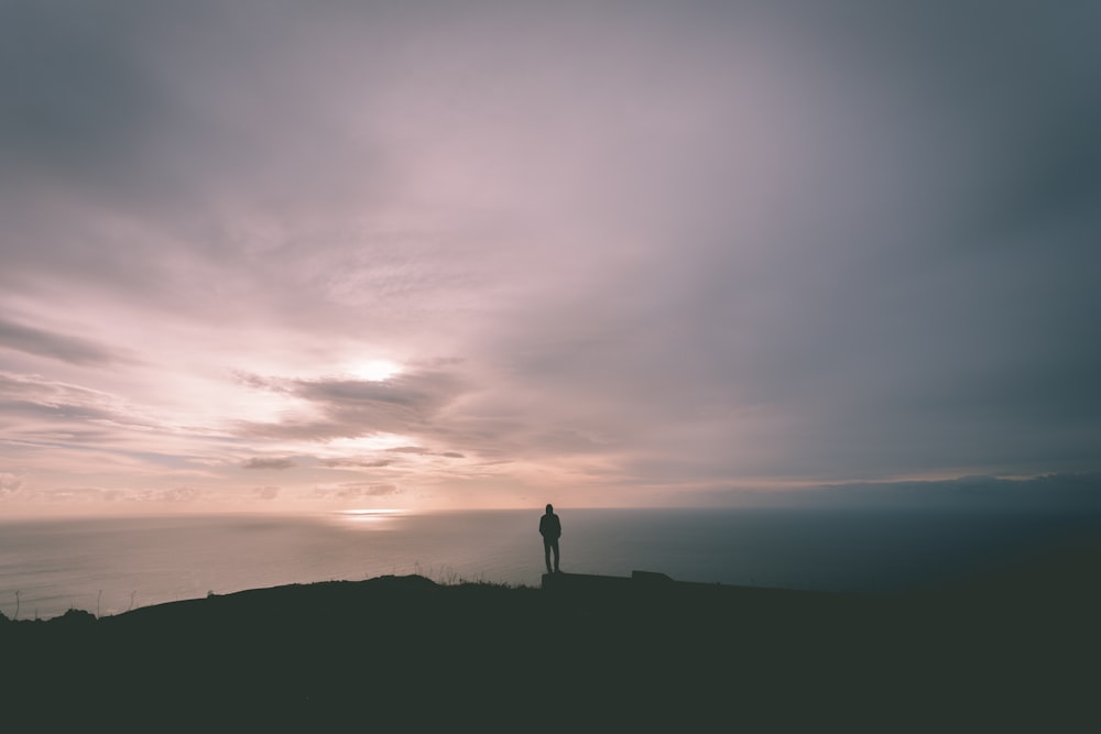 person standing on hill under gray sky