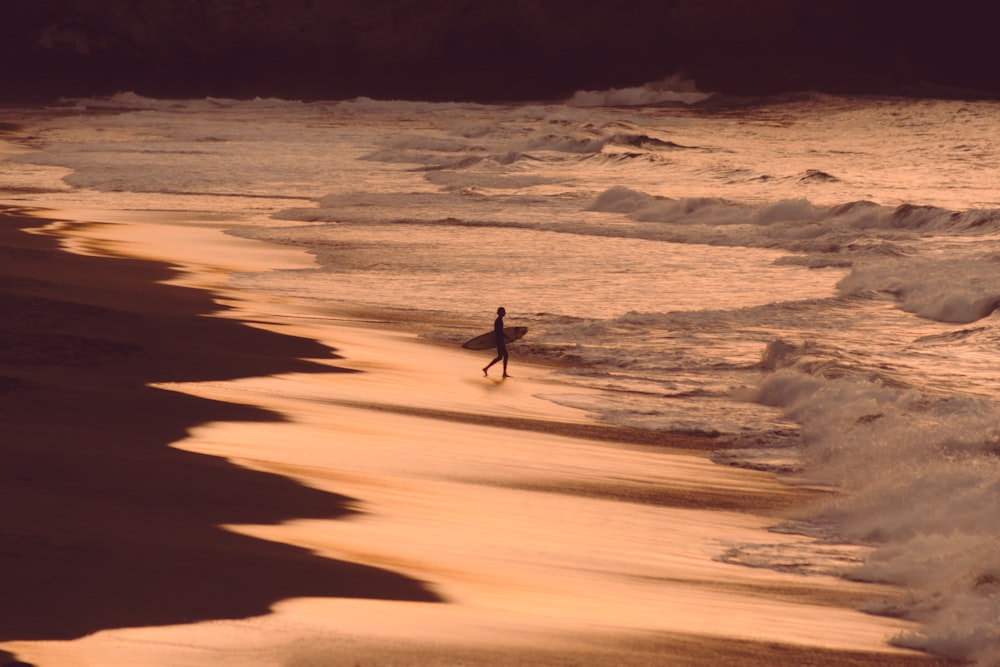 Person mit Surfbrett am Meeresufer während der goldenen Stunde