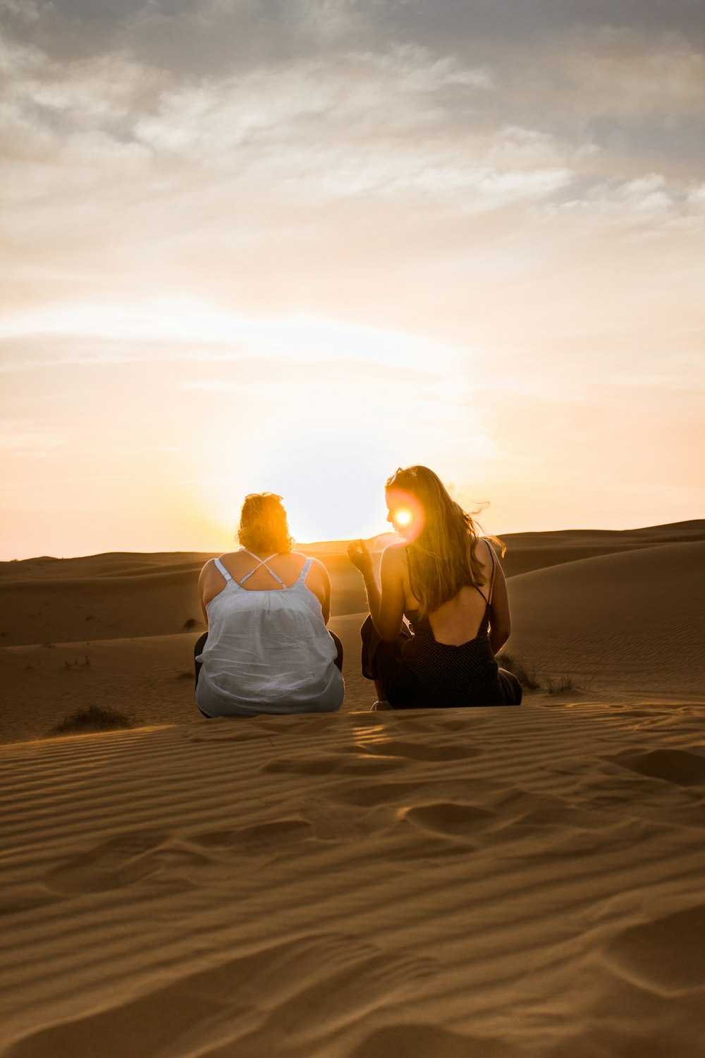 two women sitting on sand dunes during orange sunset