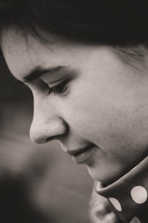 A close-up profile of a person's face, revealing delicate features and a serene expression. The black and white composition accentuates the texture of the skin and hair, creating an intimate and contemplative atmosphere.