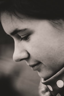 A close-up profile of a person's face, revealing delicate features and a serene expression. The black and white composition accentuates the texture of the skin and hair, creating an intimate and contemplative atmosphere.