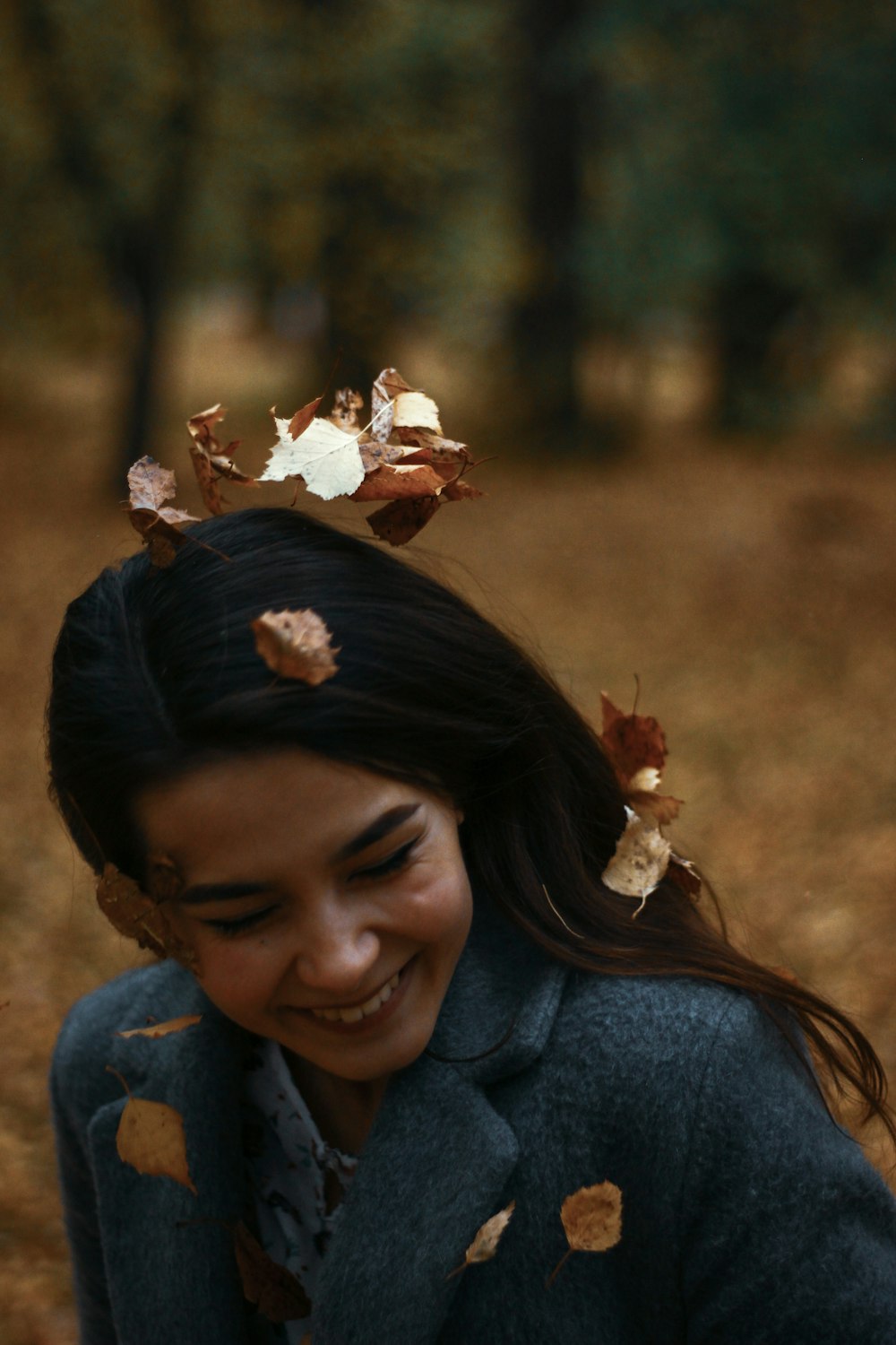 smiling woman in blue coat with leaves on her head