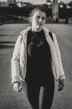 Model walking in a quiet urban street wearing layered neutral clothing.