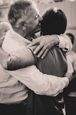Two individuals are embracing each other warmly, conveying a sense of closeness and affection. The setting appears to be informal, with an intimate and friendly atmosphere.