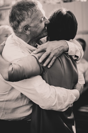 Two individuals are embracing each other warmly, conveying a sense of closeness and affection. The setting appears to be informal, with an intimate and friendly atmosphere.
