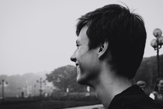 A black and white profile portrait of a person with short hair, smiling and looking towards the left. In the background, there is a foggy park scene with trees and lampposts.