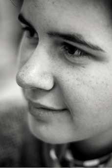 A close-up, black and white portrait of a person's face, focusing on the eyes, nose, and mouth. The lighting highlights the texture of the skin and the expression is calm and introspective.